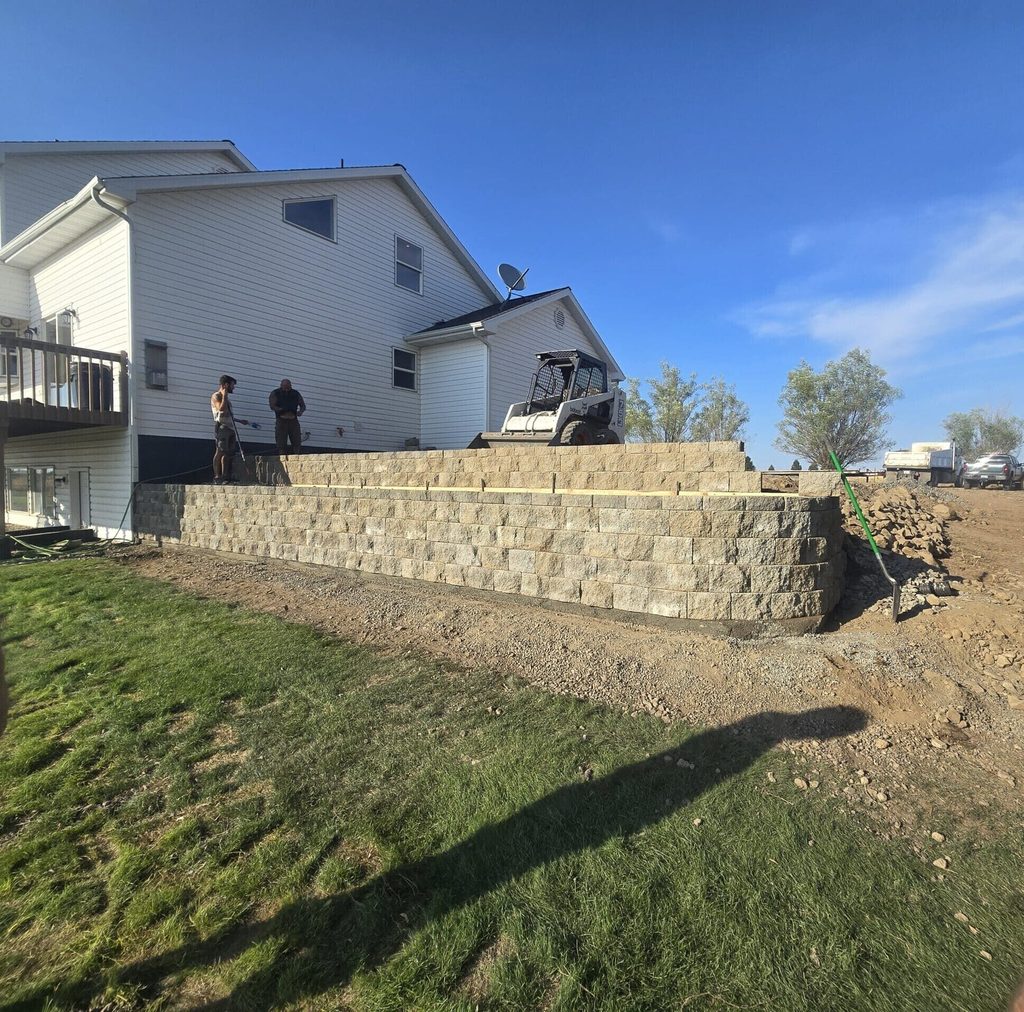 Block retaining wall being built beside a house with a skid steer